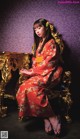 A woman in a red kimono sitting on a gold chair.