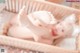 A baby laying in a wicker basket with her feet up.