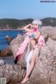 A woman in a bikini sitting on a rock by the ocean.