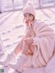 A woman sitting on a bed in the snow wearing a white coat and hat.