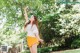 A woman in a white shirt and yellow skirt standing under a tree.