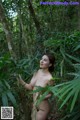 A naked woman standing in the middle of a forest.