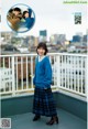 A woman in a blue sweater and plaid skirt standing on a balcony.