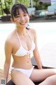 A woman in a white bikini sitting by a pool.