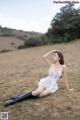 A woman in a white dress and black boots sitting in a field.