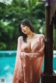 A woman in a pink dress leaning against a pole by a pool.