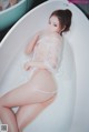 A woman in a white lingerie sitting in a bathtub.