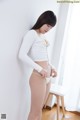 A woman in a white shirt and yellow panties leaning against a wall.