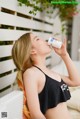 A woman in a black bikini drinking from a bottle.