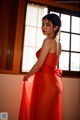 A woman in a red dress standing in front of a window.