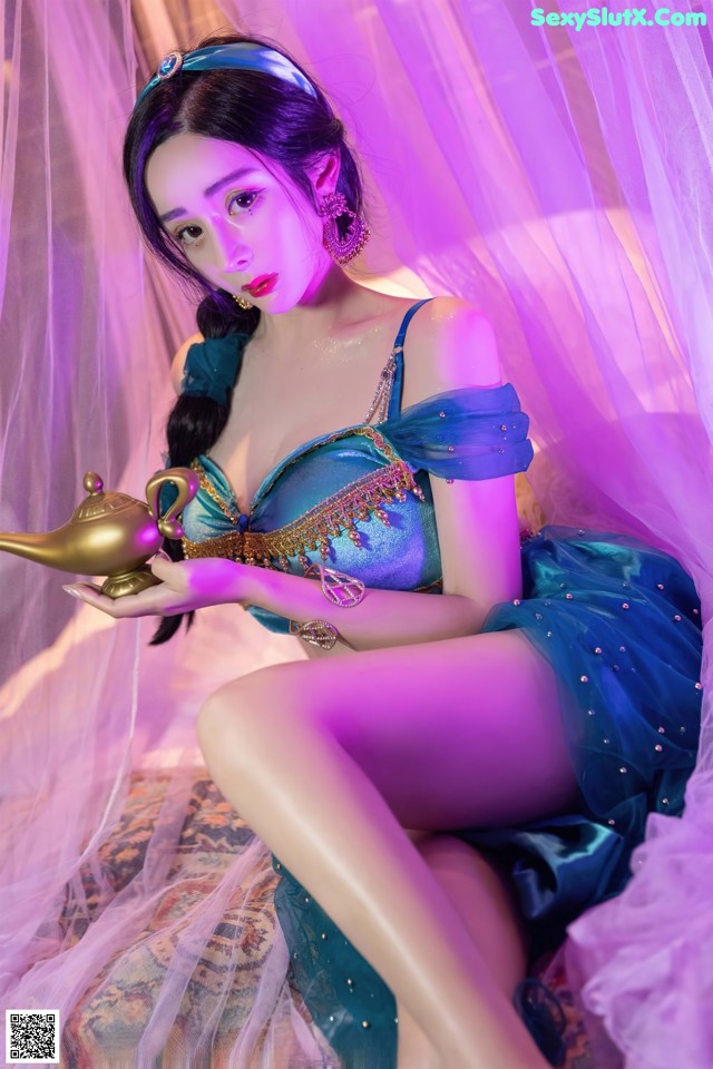 A woman in a blue dress sitting on a bed holding a lamp.