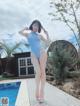 A woman in a blue swimsuit standing next to a swimming pool.