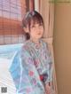 A woman in a blue kimono sitting by a window.