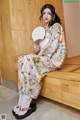 A woman in a kimono sitting on a bench holding a fan.