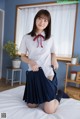 A woman in a school uniform is sitting on a bed.