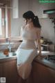 A woman in a white dress sitting on a kitchen counter.