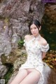 A woman in a white dress sitting on a rock by a river.