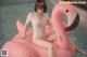 A woman sitting on an inflatable flamingo in a pool.