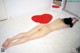 A naked woman laying on a white rug with a red heart on it.