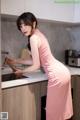 A woman in a pink dress standing in a kitchen.